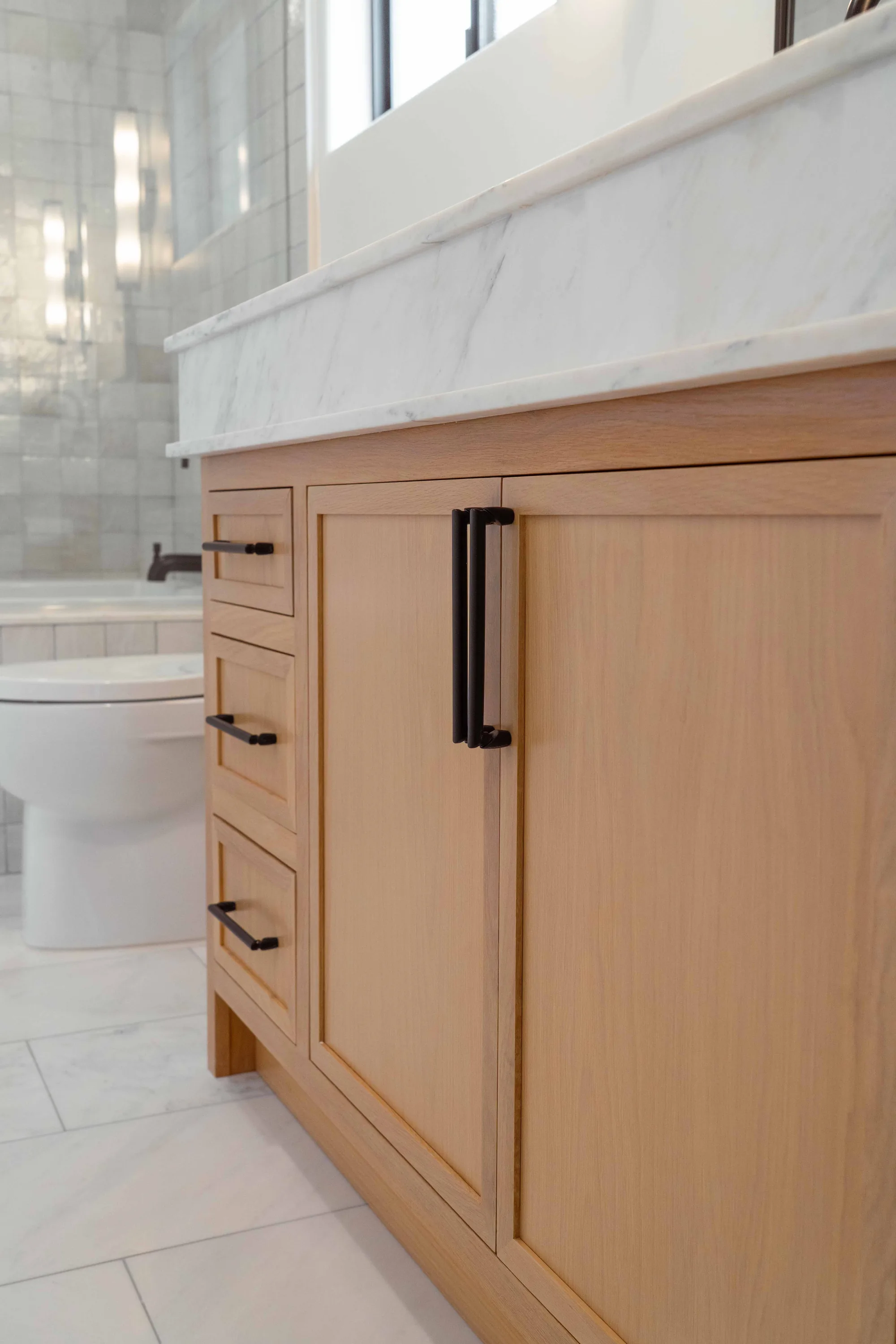 Bathroom vanity closeup showing white oak cabinet doors, marble countertop, and matte black hardware