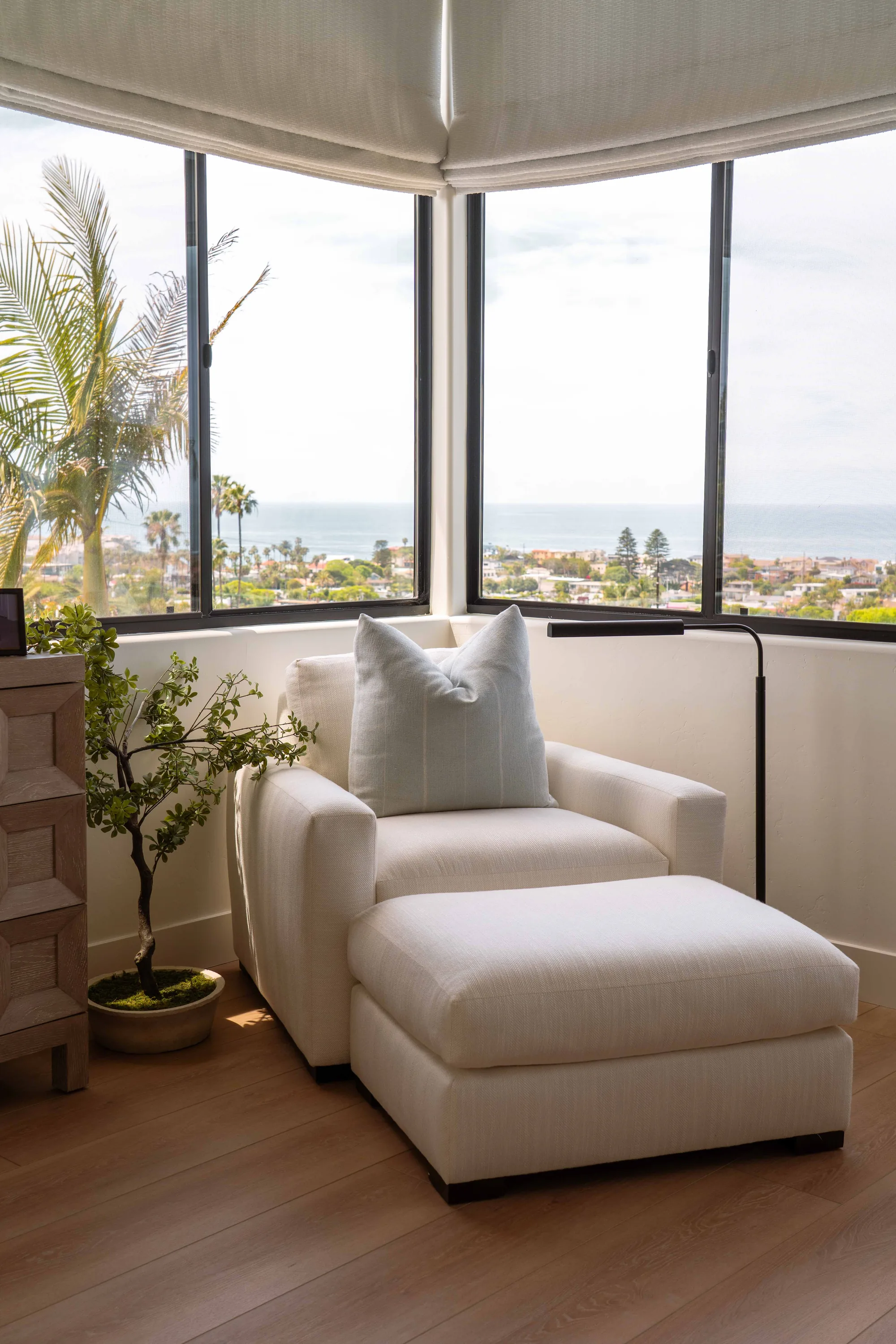 Reading nook in Solana Beach bedroom with corner windows overlooking the Pacific Ocean and palm trees