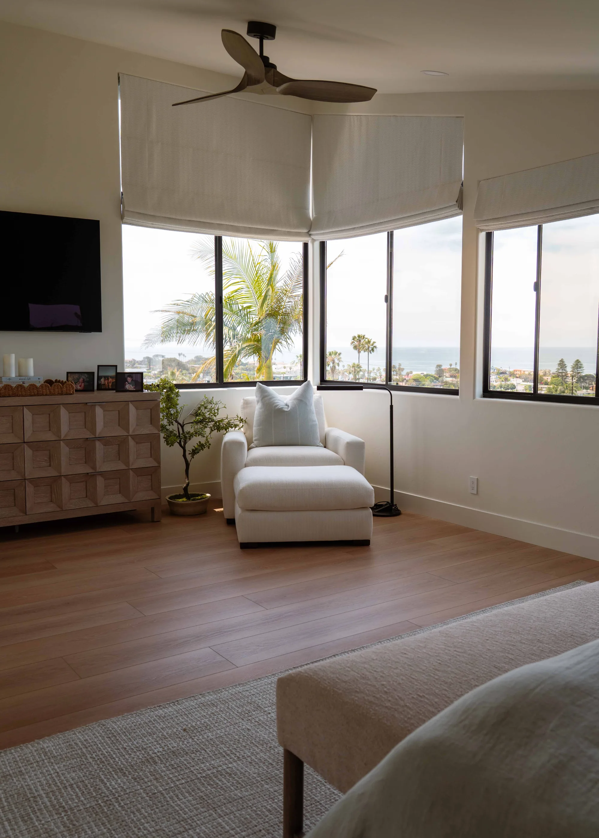 Primary bedroom with panoramic ocean view windows, wide-plank hardwood floors, and ceiling fan in Solana Beach remodel