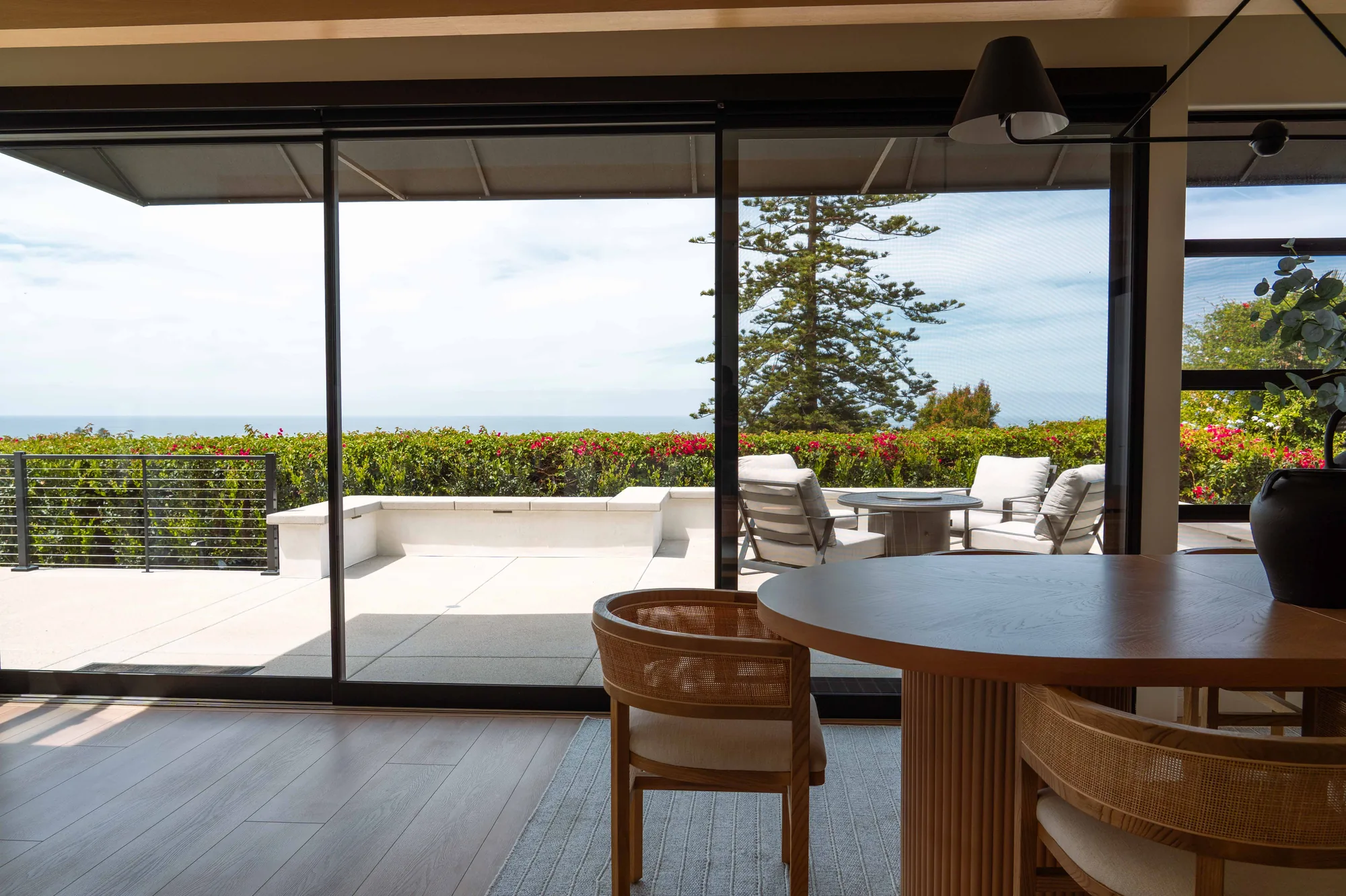 Dining area with round table, rattan chairs, and floor-to-ceiling glass looking out to terrace and ocean in Solana Beach
