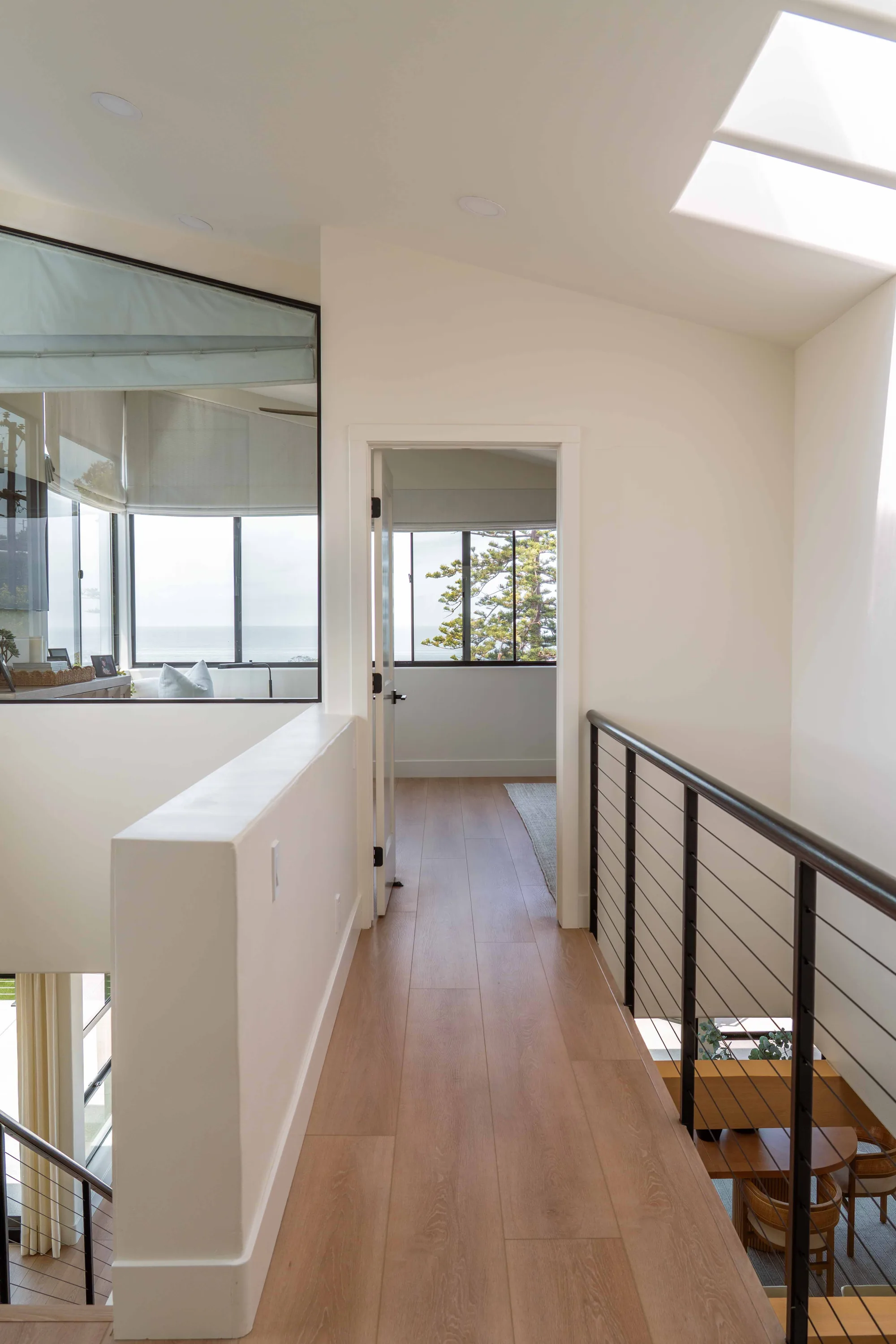 Upper hallway in Solana Beach remodel with skylight, cable railing, and wide-plank hardwood flooring