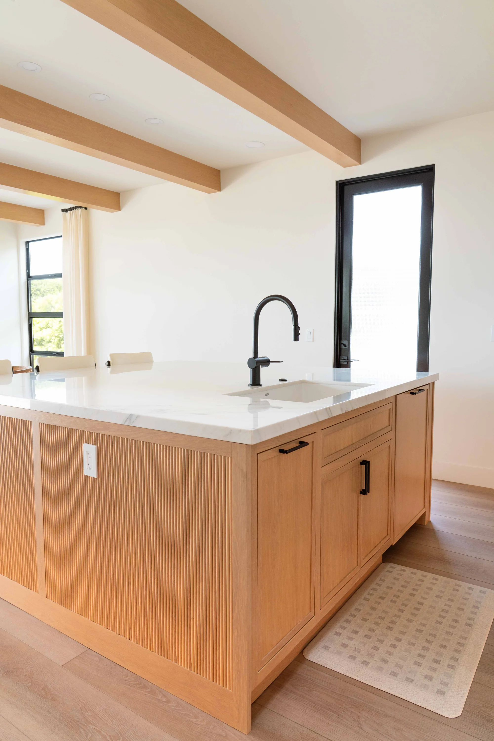 Kitchen island with natural white oak fluted panel base, quartz countertop, and matte black gooseneck faucet