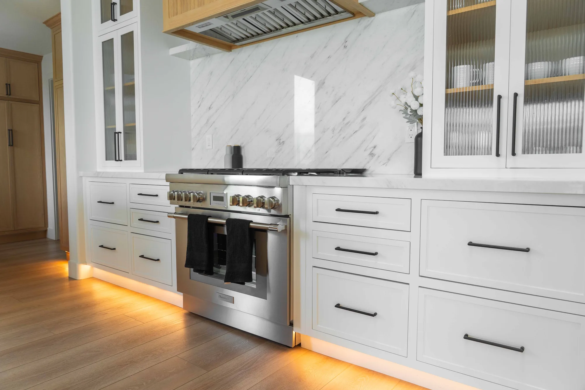 Kitchen cooking wall in Solana Beach remodel with white shaker cabinets, professional range, marble slab backsplash, and LED under-cabinet lighting