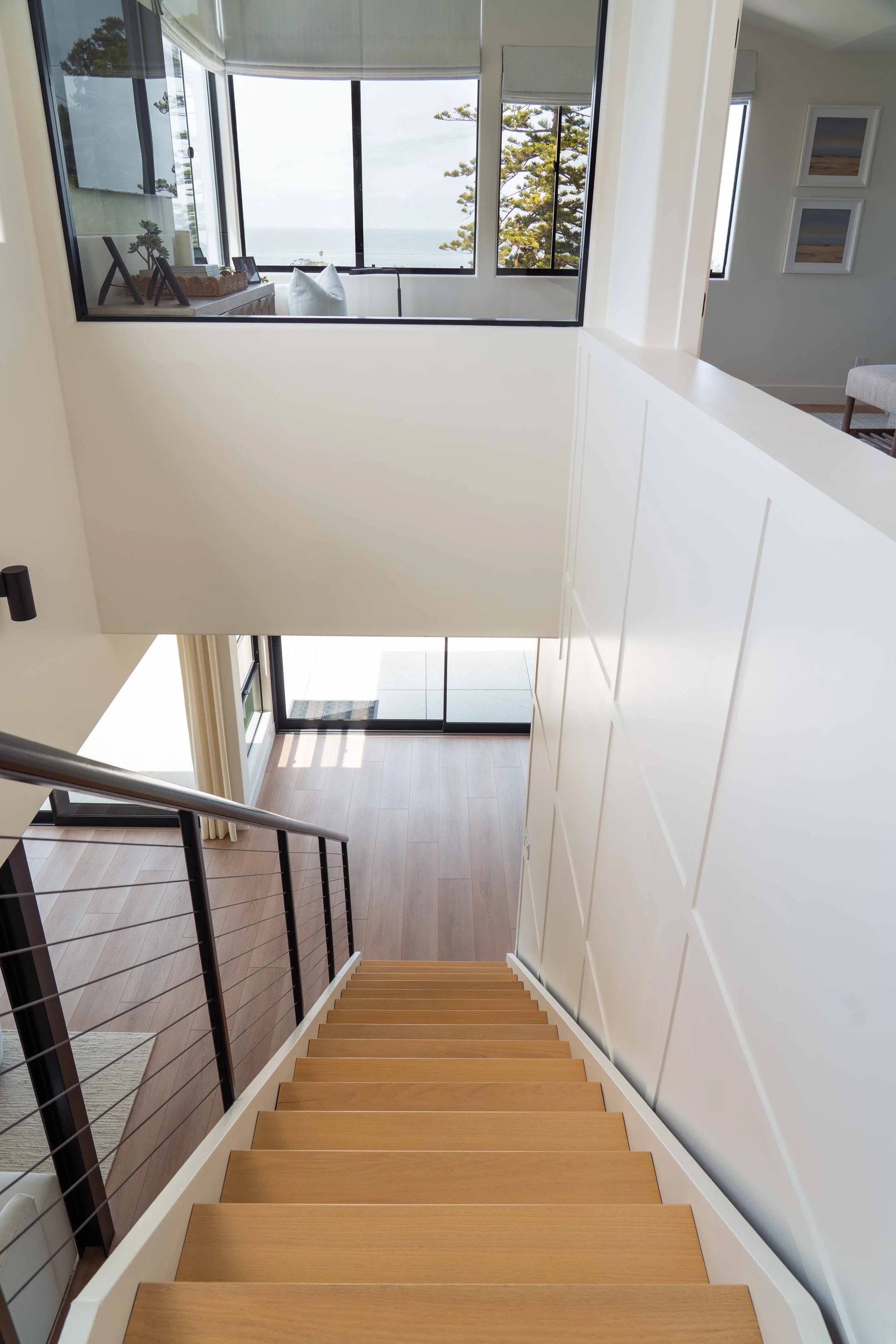 Modern staircase in Solana Beach home with natural wood treads, cable railing, and ocean view through windows