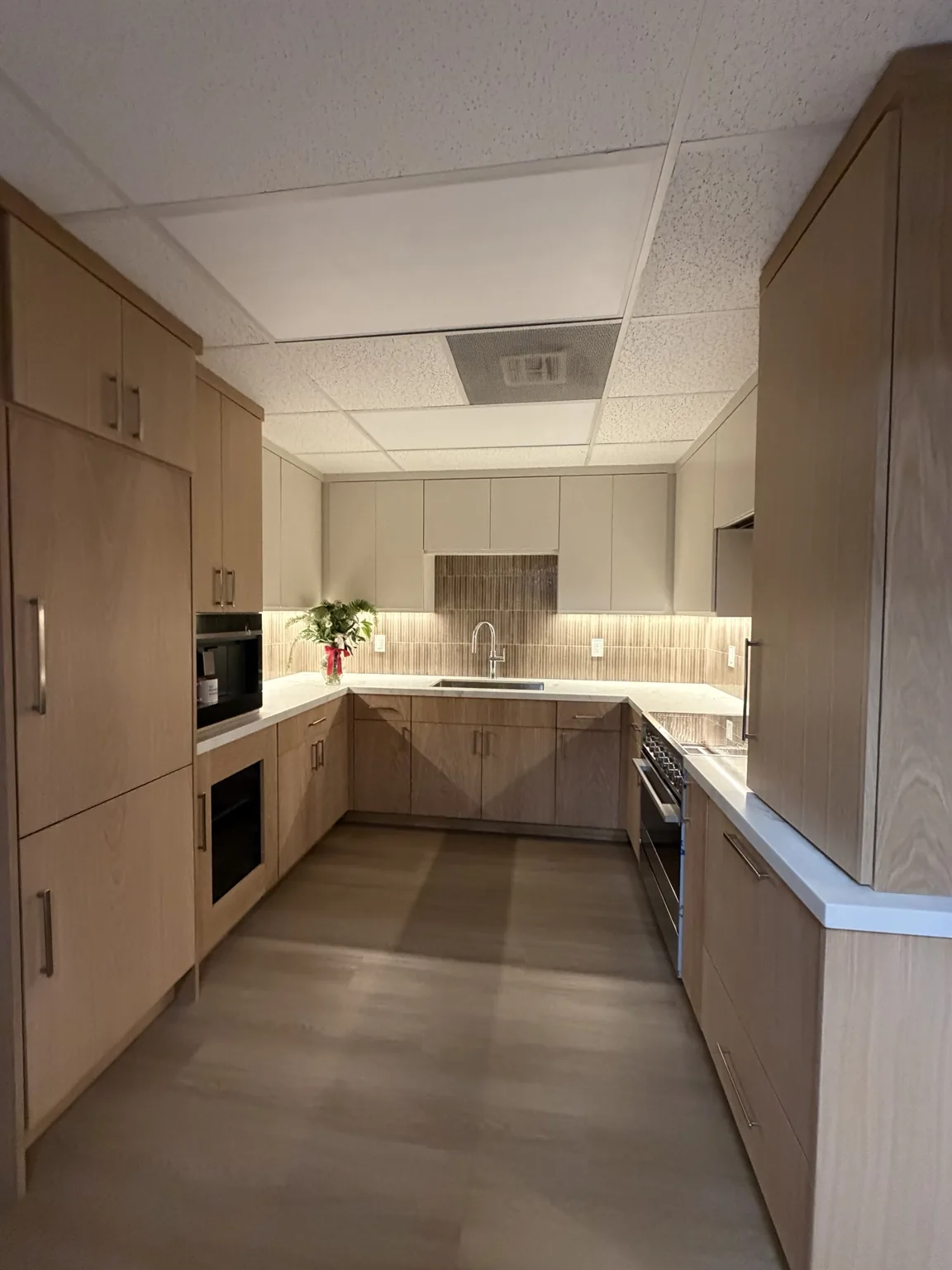 Display kitchen with oak slab-front cabinetry, white upper cabinets and a vertical tile backsplash