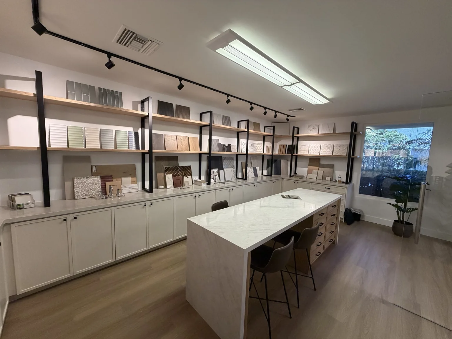 Materials studio with tile and wood samples on open shelving above white cabinetry, and a marble waterfall island