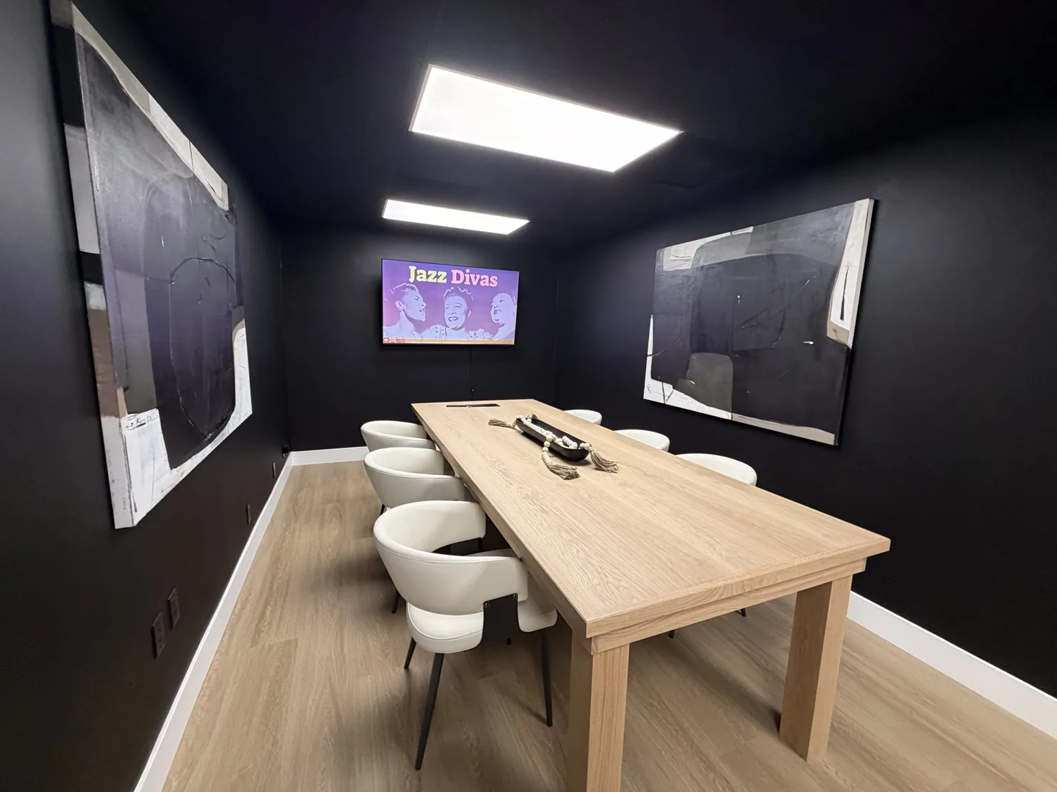 Meeting room with a light oak table, white upholstered chairs and large abstract artwork