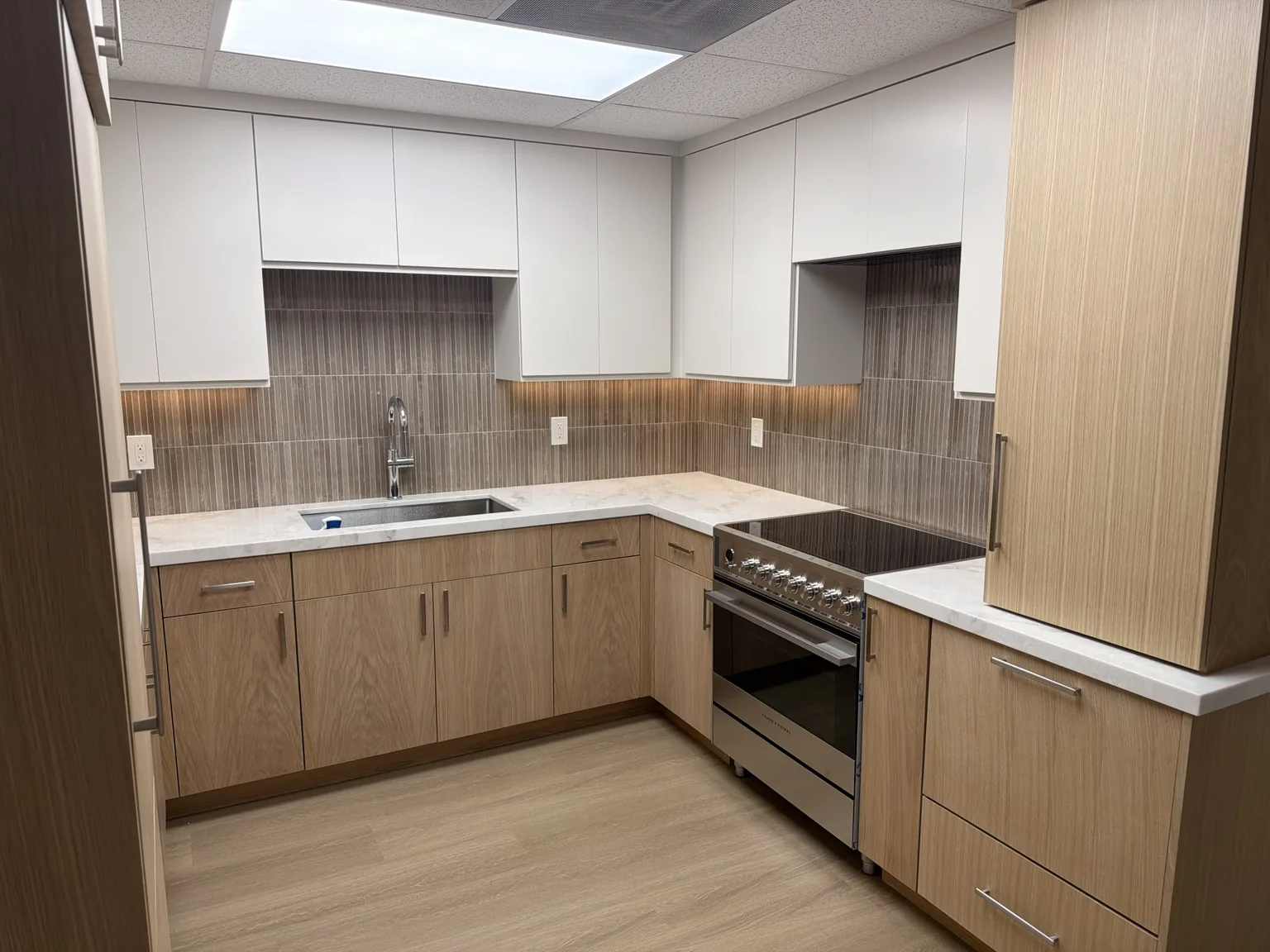 Design Center display kitchen with oak slab-front base cabinets, white flat-panel uppers and a stainless range
